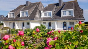 A two-story house with a symmetrical facade, multiple chimneys, and a well-maintained garden with pink flowers. - Sönshörn 20 - Holiday apartment "Sönshörn 20" in Munkmarsch (Munkmarsch)