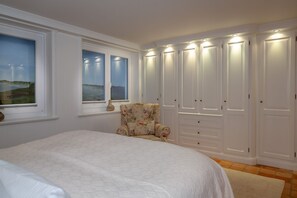 Une chambre avec un grand lit, une chaise, une armoire et une fenêtre donnant sur un beau paysage.