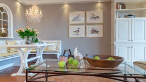 A dining area with a glass table, white furniture, a chandelier, and framed bird paintings on the wall. - Sönshörn 20 - Holiday apartment "Sönshörn 20" in Munkmarsch (Munkmarsch)
