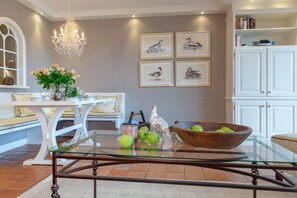 Un coin repas avec une table en verre, des meubles blancs, un lustre et des tableaux représentant des oiseaux, accrochés au mur.