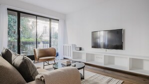 A modern living room with a sofa, armchair, and a flat-screen TV mounted on the wall. - Blueground | Porte Maillot. balcony & concierge (Paris)