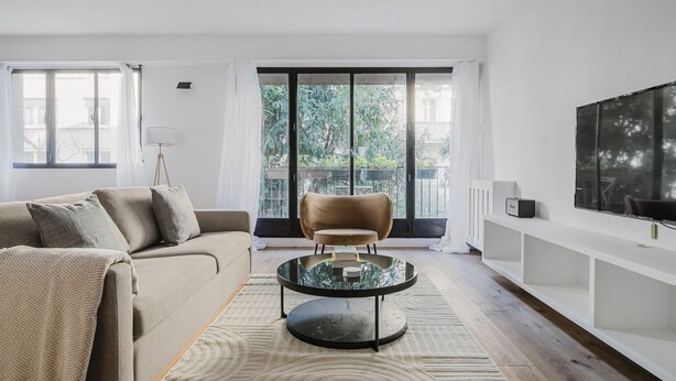 A modern living room with a sofa, a round glass coffee table, a chair, a TV, and a balcony with plants. - Blueground | Porte Maillot. balcony & concierge (Paris)