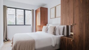 A bedroom with a bed, wooden wardrobe, and a window with curtains. - Blueground | Porte Maillot. balcony & concierge (Paris)