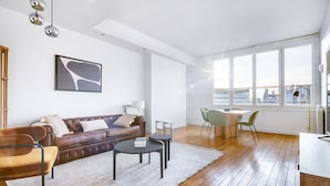 Una sala moderna con un sofá de cuero, una mesa de centro y un comedor con sillas. Hay un ventanal que ofrece vistas de la ciudad.