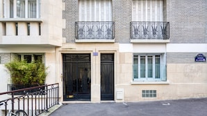 Un edificio de varios pisos con entrada a nivel de calle, un pequeño balcón con barandillas de metal negro ornamentadas y un letrero que indica el nombre de la calle.