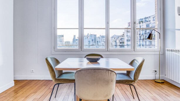 Un comedor con una mesa, cuatro sillas, un ventanal y vista a la ciudad, además de una lámpara de pie.