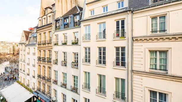 Una hilera de edificios de varios pisos con balcones, ventanas amplias y vista a la calle.