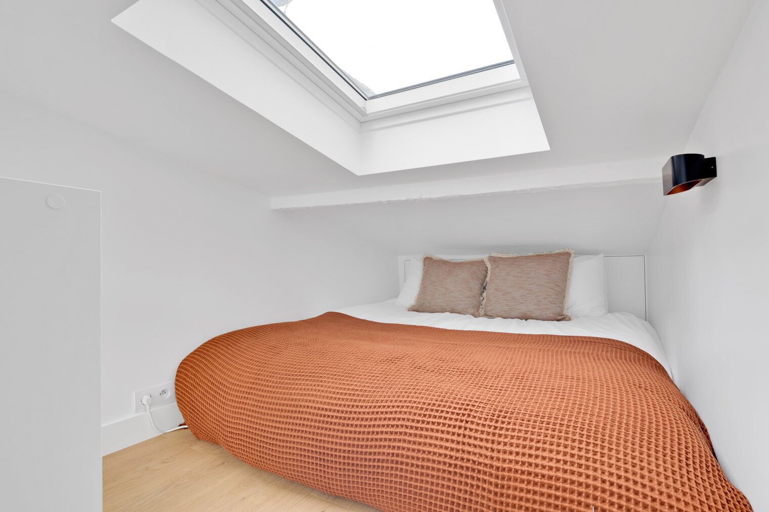 A modern bedroom with a skylight, a bed with a patterned blanket, and a bedside table.