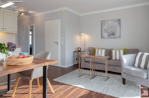 A modern living room with a dining area, grey sofa, and a painting on the wall. - Strandläufer A3 - Holiday apartment "Strandläufer A3" in Wenningstedt for two (Wenningstedt-Braderup (Sylt))