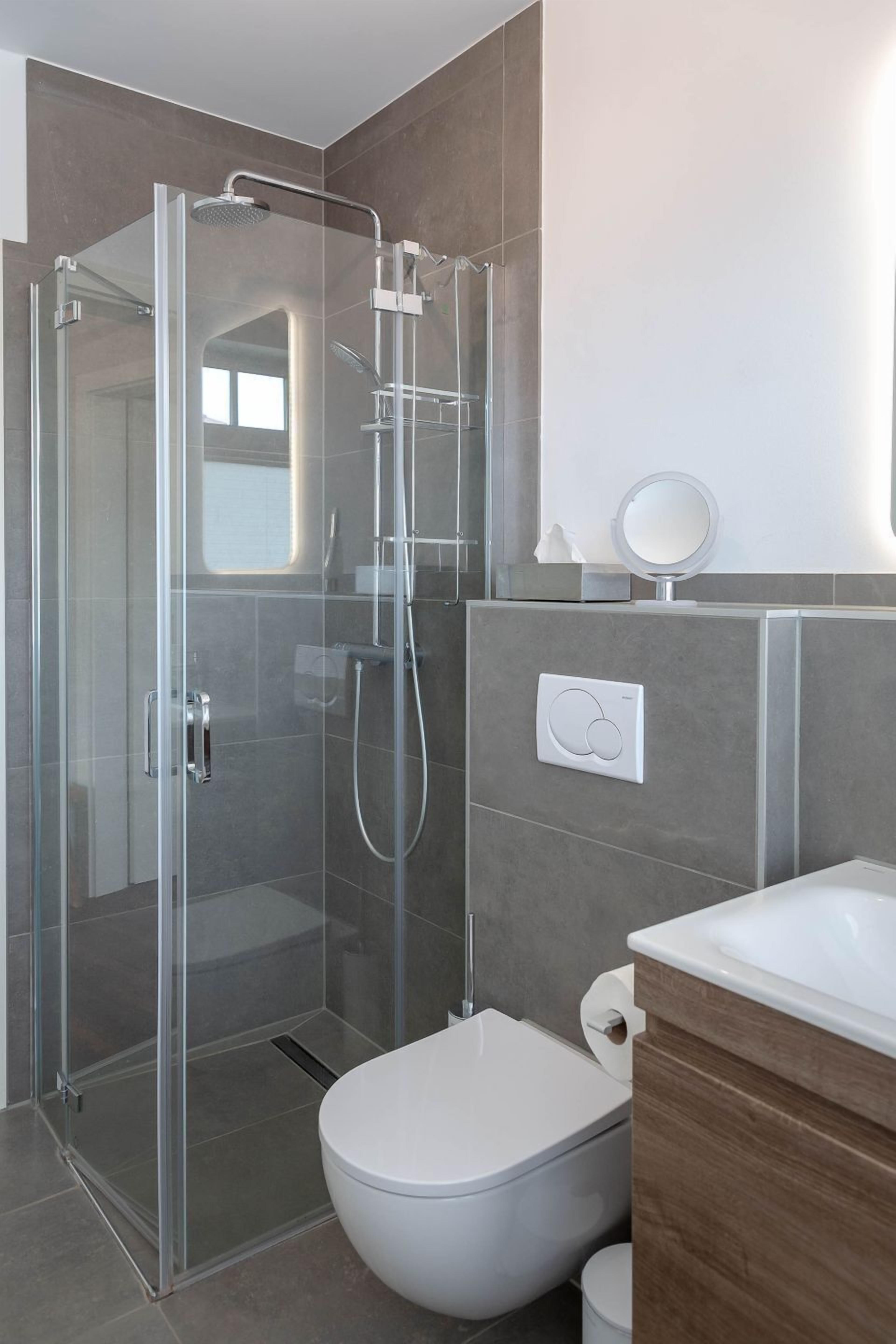 A modern bathroom with a glass-enclosed shower, a toilet, and a vanity with a mirror.