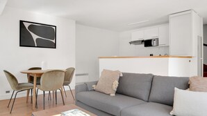 En moderne stue med en grå sofa, et træsofabord med en bog, og et spiseområde med et lille bord og stole.