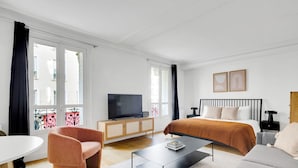 Una habitación de hotel moderna con cama, sofá, sillón, televisor y una mesita.