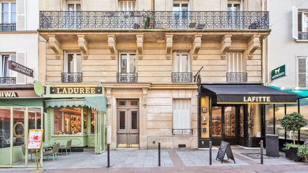 Vista de la calle de los restaurantes Laduree y Lafitte, frente a un edificio clásico con balcones.