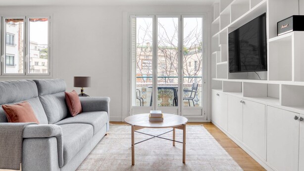 A modern living room with a grey sofa, a small round coffee table, and a TV on a white cabinet. - Blueground | Michel-Ange Molitor, near tennis (Paris)