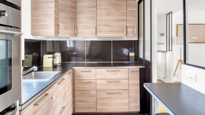 A modern kitchen with wooden cabinets, a stainless steel countertop, and a built-in oven. - Blueground | Michel-Ange Molitor, near tennis (Paris)