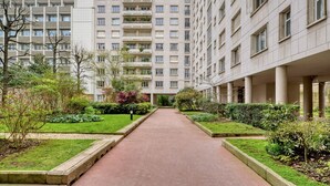 A multi-story residential building with a central pathway flanked by greenery and a covered walkway on the right. - Blueground | Michel-Ange Molitor, near tennis (Paris)