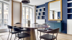 A dining area with a round table, six chairs, a vase, and a large mirror on the wall. - Blueground | Rambuteau, elevator, nr Chatelet mall (Paris)