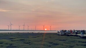 A sunset with wind turbines in the background and a crowd on a viewing platform.