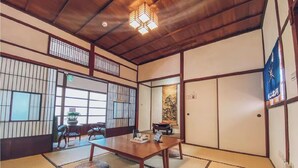 A traditional Japanese room with tatami flooring, sliding doors, a low wooden ceiling, and a hanging light fixture.