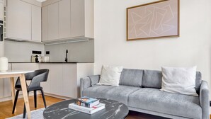 A modern living room with a grey sofa, a round black coffee table, and a minimalist kitchen in the background. - Blueground | Louvre, nr Rue Rivoli shops (Paris)