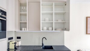 A modern kitchen with open shelving, a black countertop, a sink, and a toaster. - Blueground | Louvre, nr Rue Rivoli shops (Paris)