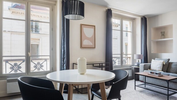 A modern living room with a round dining table, black chairs, a white vase, and a grey sofa.
