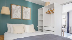 A bedroom with a bed, two framed artworks, a wardrobe, and a hanging rack.