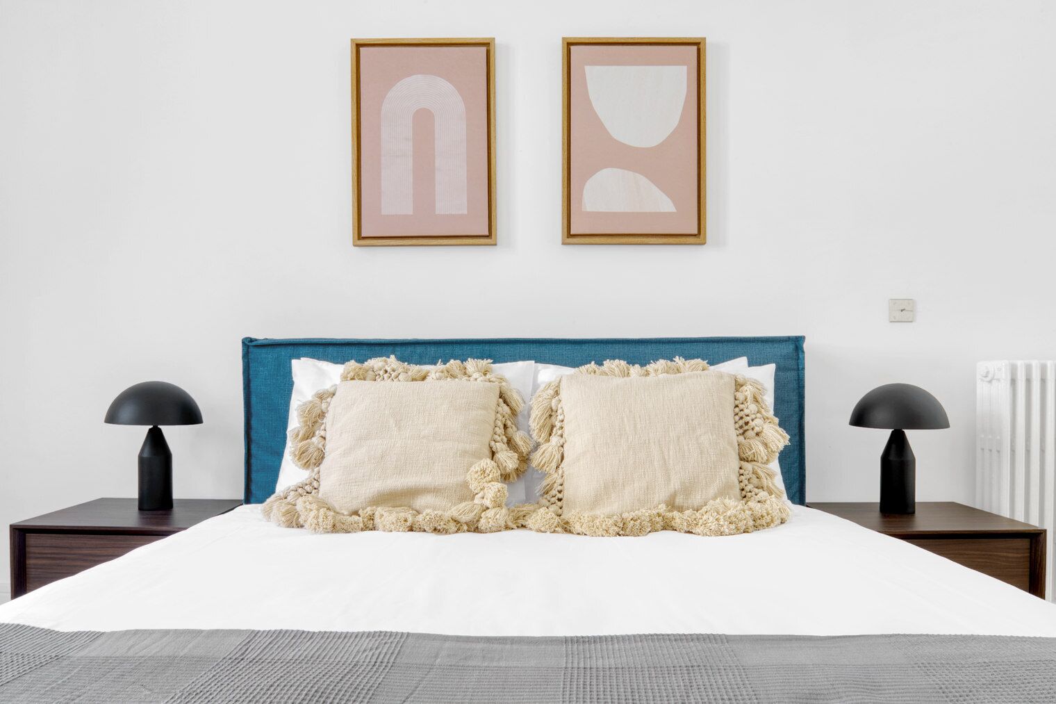Ein ordentlich bezogenes Bett mit zwei Kissen, einem blauen Kopfteil und zwei Nachttischlampen.