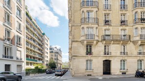 Une vue de rue montrant une rangée d’immeubles résidentiels à plusieurs étages, dotés de balcons, avec des voitures garées et un ciel dégagé.