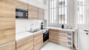 Une cuisine moderne avec des meubles blancs, un four à micro-ondes de marque Bosch, un évier et une fenêtre avec des barreaux.