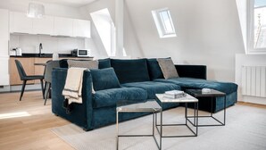 A modern living room with a dark blue sofa, a small coffee table, and a kitchen area in the background. - Blueground | Le Marais, renovated, furnished (Paris)