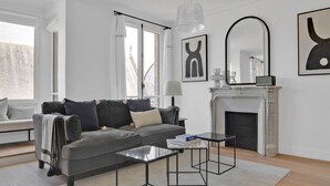 A modern living room with a grey sofa, two black coffee tables, a fireplace, and abstract art on the walls. - Blueground | Le Marais, furnished & equipped (Paris)