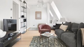 En moderne stue med et fladskærms-tv, en lyserød lænestol, en grå sofa og et mønstret tæppe.