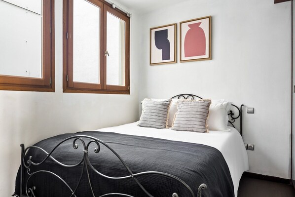 A bedroom with a bed, two windows, and two framed artworks on the wall.