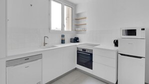 Moderni keittiö, jossa on valkoiset kaapit, astianpesukone, uuni, mikroaaltouuni ja kahvinkeitin.