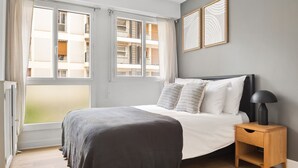 Une chambre à coucher avec un lit, une table de chevet, une lampe et deux fenêtres.