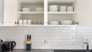 Une cuisine avec des meubles blancs, un plan de travail recouvert de carreaux, un évier et une machine à café.