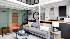 A modern living room with a grey sofa, a small round table, and a bookshelf. - Blueground | Monceau, furnished, near park (Paris)