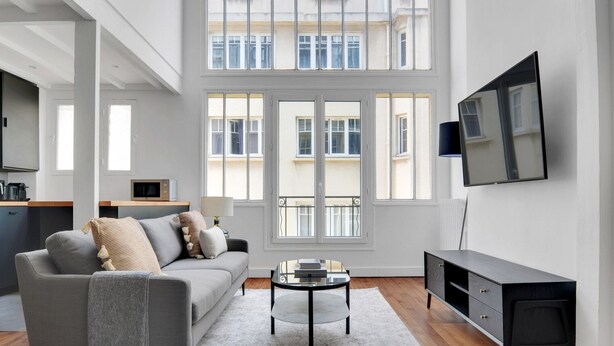 A modern living room with a grey sofa, a coffee table, and a TV on the wall. - Blueground | Monceau, furnished, near park (Paris)