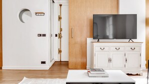 Een moderne woonkamer met een flatscreen televisie op een witte kast, een houten deur en een witte muur met een ronde uitsparing.