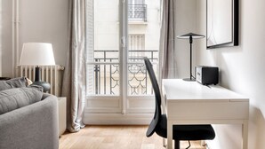 Een moderne hotelkamer met een wit bureau, een zwarte stoel, een grijze bank, een lamp en een radiator.