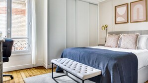 Een slaapkamer met een bed, een bankje, een bureau en een raam.