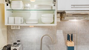 A kitchen with a modern design, featuring a stainless steel sink, a glass shelf with white dishes, and a toaster. - Blueground | Argentine, elevator, nr Porte Maillot (Paris)