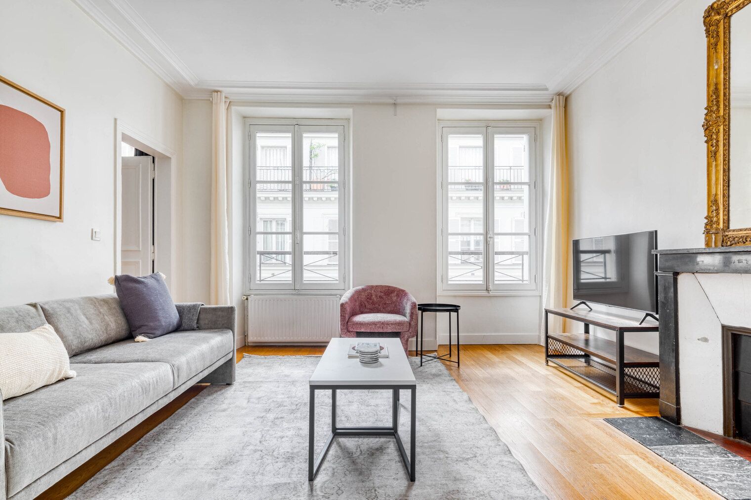 Ein modernes Wohnzimmer mit grauem Sofa, einem pinken Sessel, einem Couchtisch, einem Fernseher und einem Kamin.