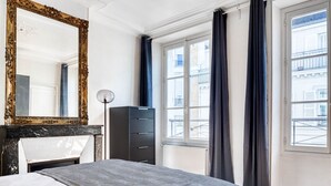 Hotellihuone, jossa on sänky, suuri peili, vaatekaappi ja ikkuna, jossa on verhot.