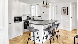 Une cuisine moderne avec des meubles blancs, un îlot central doté de tabourets et un luminaire suspendu.