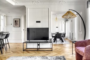 Relax in this stylish living room with a large flat-screen TV, herringbone-patterned floor, and comfortable seating area.