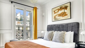 Une chambre d’hôtel avec un grand lit, une vue sur la ville depuis un balcon et une peinture abstraite moderne accrochée au mur.