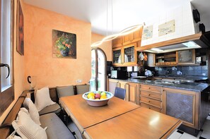Una cocina con armarios de madera, una mesa de comedor con un frutero y un banco con almohadones.