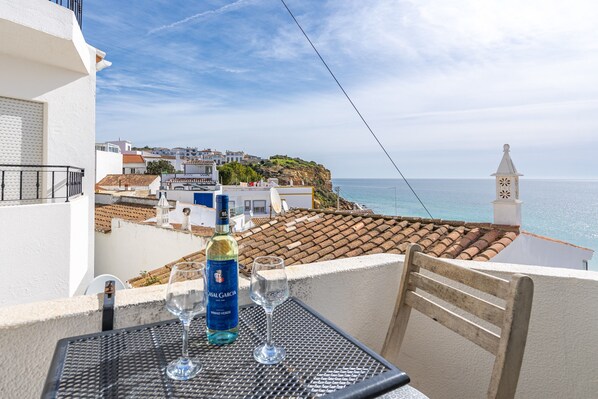 A balcony with a table, two wine glasses, and a bottle of Casal Garcia wine. - Apartment 'Vista Mar - Burgau' with Sea View, Balcony and Wi-Fi (Burgau)
